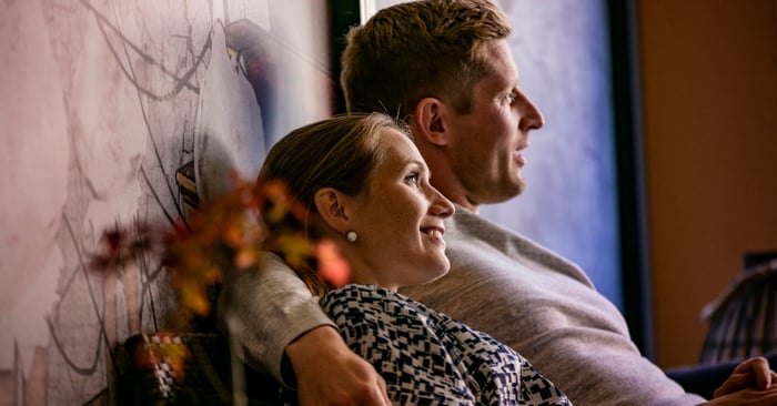 mies ja nainen istuvat mukavasti sohvalla ja hymyilevät