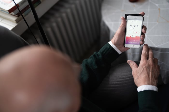Miehellä on puhelimessa Wattisen mobiilisovellus, jossa näkyy lämpötilaluku 17. 